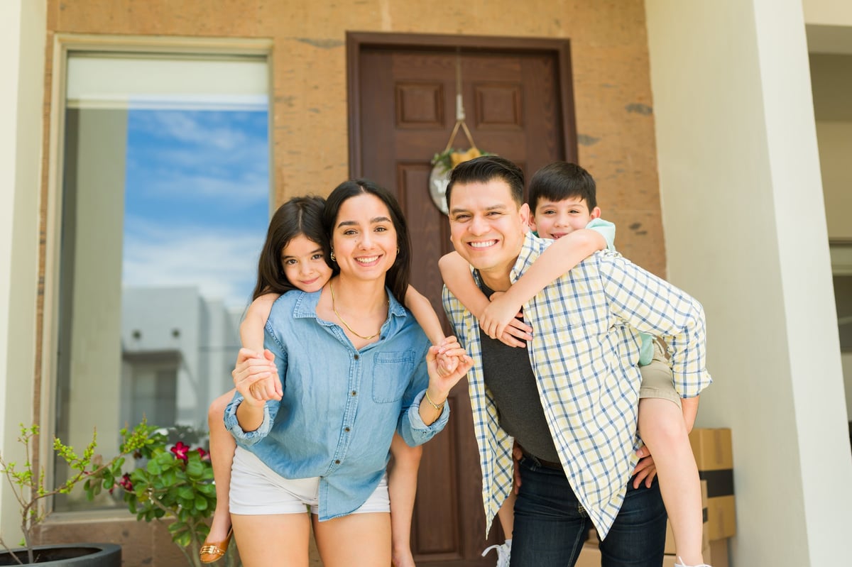 Happy mom and dad piggybacking their kids having fun in the entryway while moving into a new house buying real estate