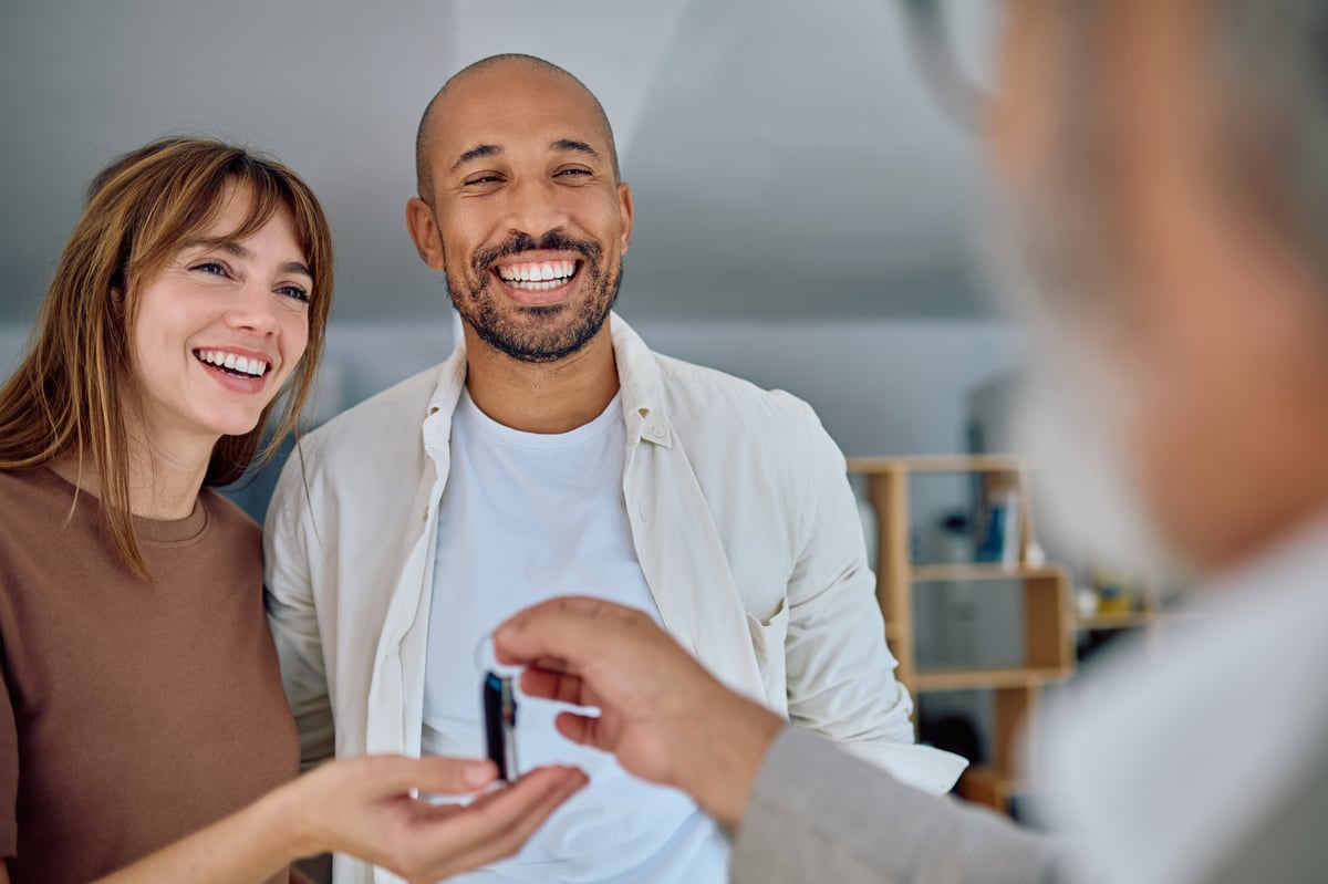 Agente inmobiliario entregando llaves de casa a nuevos propietarios sonrientes tras cerrar trato exitoso